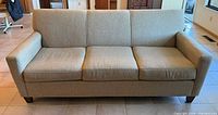 Front view of light beige 3-cushion sofa on tile floor