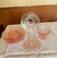 Group shot showing all pink Depression glass pieces: stack of swirl plates, vertical display plate, compote bowl, handled dish