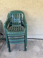 Front view of four stacked green plastic patio chairs showing slotted back design