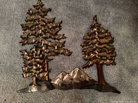 Full view of metal wall sculpture showing trees and mountain design