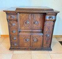 Closed walnut cabinet showing carved floral drawer fronts and doors