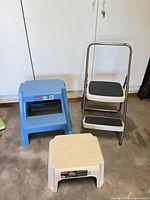 All three items: Cosco ladder, blue two-step Rubbermaid stool, beige single-step Rubbermaid stool
