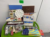 Overview of books, palettes, boxed paints and brushes on green surface