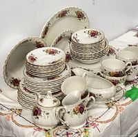 Full set grouped on tablecloth showing plates, bowls, cups, serving pieces
