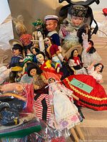 pile of assorted small dolls in various costumes with bag of clothing