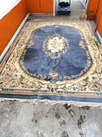 Full view of blue wool floral rug on floor showing overall design and fringe