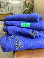 Stack of four blue moving blankets showing overall appearance and tears on top blanket