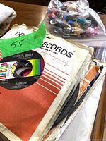 Stack of 45 RPM records in sleeves with bag of unrelated items in background