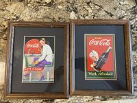 Two framed Coca-Cola advertising prints on countertop