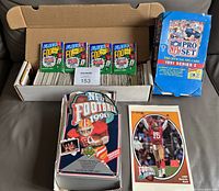 Cardboard storage box filled with trading cards, four sealed 1991 Fleer wax packs, empty 1991 Pro Set Series 1 box, Joe Montana oversized card and promotional insert visible