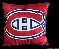 Front view of red plush pillow featuring Montreal Canadiens logo, shows fabric texture and blue piping