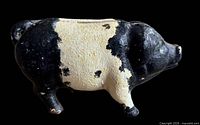 Left side view of black and white cast iron pig bank showing slot and paint wear