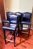 Four black faux-leather counter bar stools grouped together
