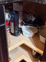 Cabinet interior with juicer, ceramic casseroles, stainless pans, cooling rack