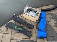 Cardboard box with duffle barbeque set and three folding chair sleeves on ground