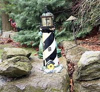 Full view of lighthouse statue among rocks and greenery