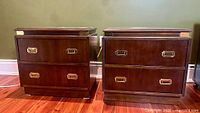 Both nightstands side by side showing overall form, two drawers each, brass pulls, brass corner brackets, plinth bases