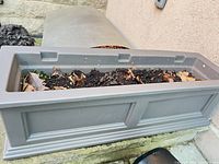 Overall view of gray plastic self-watering planter with soil inside