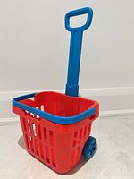 Overall view of red plastic basket with blue handle and wheels