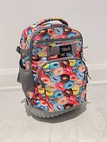 Front view of Tilami rolling backpack showing donut print, zip compartments, mesh side pocket and wheel base