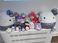 Group shot of entire Squishmallow assortment arranged on radiator, displaying size range and tag presence