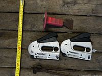 Two staple guns, red-handled chisel, brake tool beside measuring tape