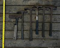 Six hammers laid out on wooden floor with tape measure for scale