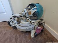 Overall view of Makita 10-inch compound sliding miter saw showing blade, arm, motor housing, fence, and dust bag