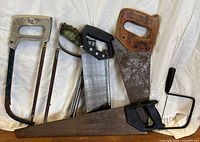 Group of five saws and separate crank handle leaning against backdrop