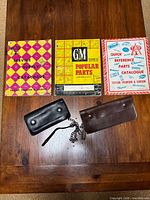 Overview of three catalogues with pink/yellow, yellow/black, and blue/red covers alongside two chain wallets (black and brown) on table