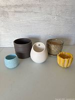 Five assorted small indoor planter pots displayed side by side