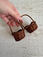 Two miniature brown wicker baskets held to show scale and weave