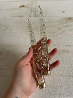 Pair of clear lucite taper candles shown in hand for scale