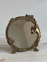 Front view of brass tabletop mirror showing female figure and floral design