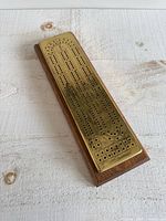 Angled top view of brass plated cribbage board on wooden base