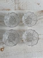 Top view of four clear cut crystal miniature bowls showing starburst pattern and scalloped edges