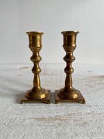 Front view of both brass candlesticks standing upright on square bases
