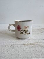 Front view of white china mug showing pink and yellow flowers and gold rim