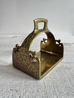 Three-quarter front view of brass stirrup tray showing handle and side engravings