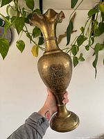 Full view of brass vase held in hand showing overall shape and etched design