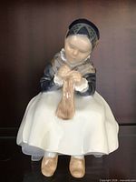 Front view of porcelain figurine seated girl knitting