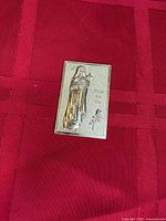 Front view of gold-tone Mary "Pray for Us" plaque on red background