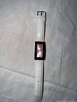 Front view of wristwatch showing dial, case and white leather strap