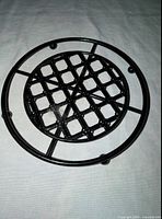 Top view of round black metal trivet showing lattice center and outer ring