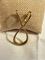 Front view of gold-tone abstract loop pendant on display pad