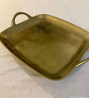 Top view of square gold-tone metal tray showing handles and surface wear