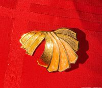 Front view showing fan-shaped goldtone scarf clip with orange enamel panels