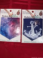 Front view of two sealed Pockets & Peekers iron-on pocket packages showing galaxy and anchor designs