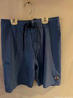 Front view of blue Billabong swim trunks hanging, showing waist drawstring, pocket, and logo patch