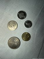 Five assorted coins on fabric surface, obverse sides visible